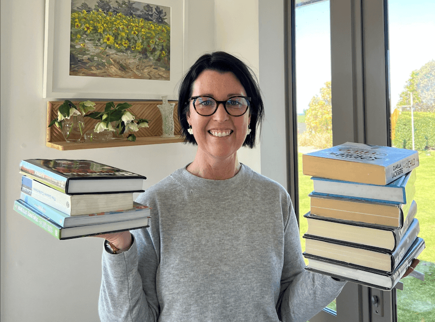 a white woman with dark hair holds a stack of books in each hand